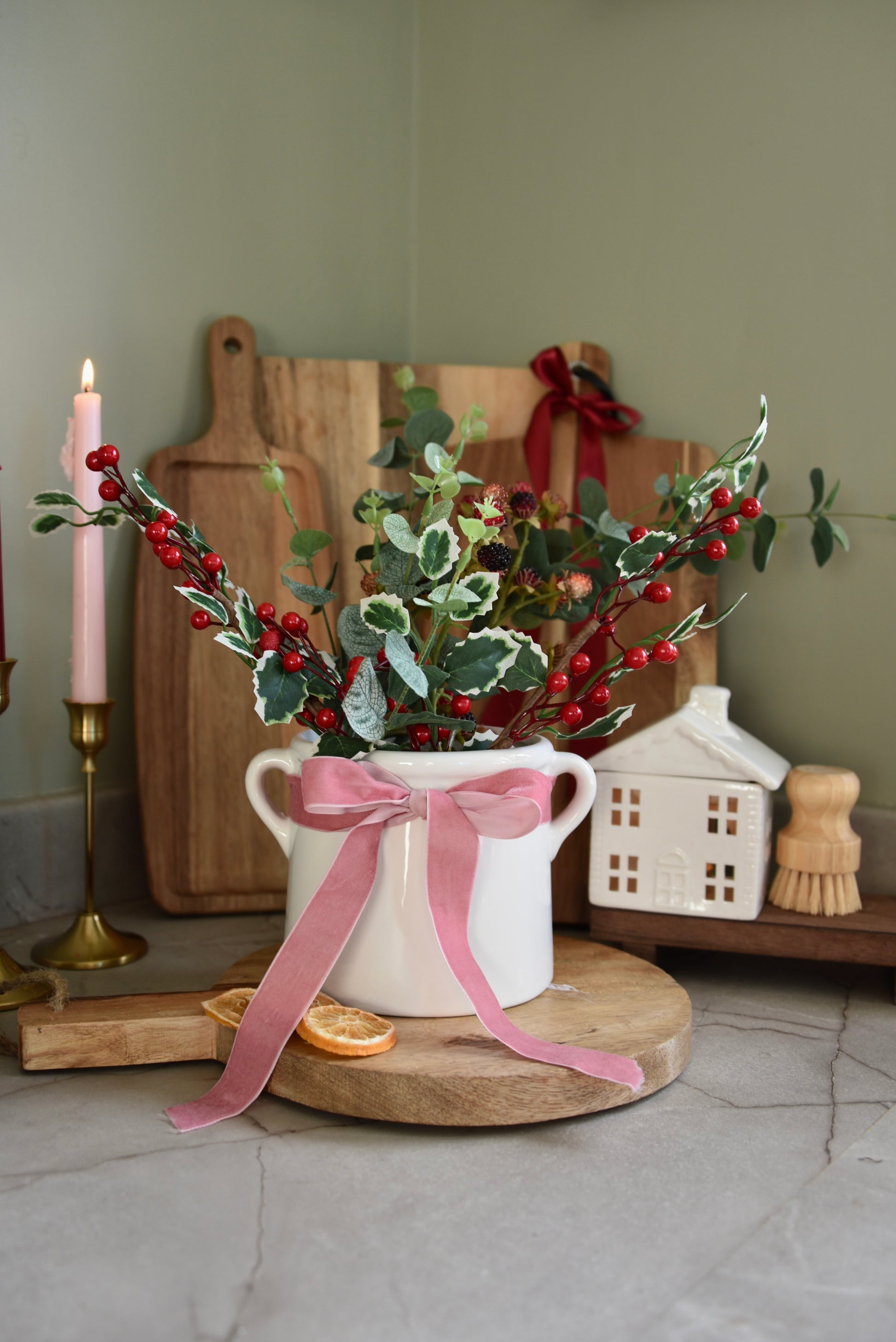 Decorative arrangement with a white vase, pink bow, and greenery on a wooden chopping board
