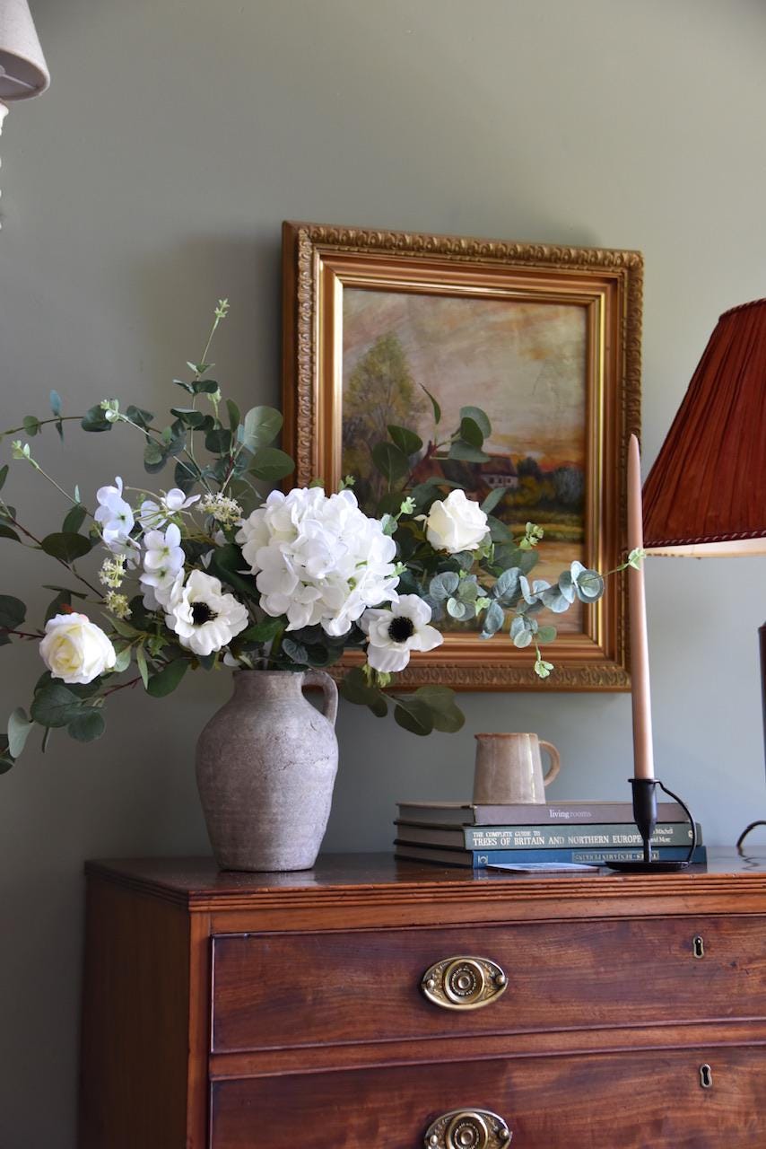 Close up of white hydrangeas, cosmos, roses and wild eucalyptus styled on a wooden table, antique oil painting in background