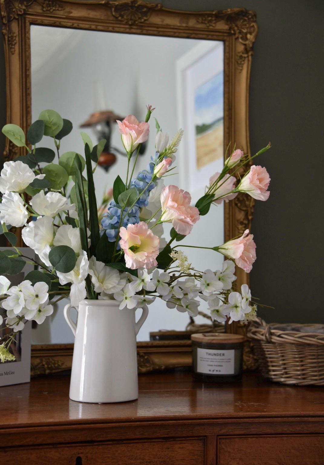 close up Wild flowers including gladiolus, wild white hydrangea, pink flowers, blue delphinium and green eucalytpus arranged in white vase on antique drawers