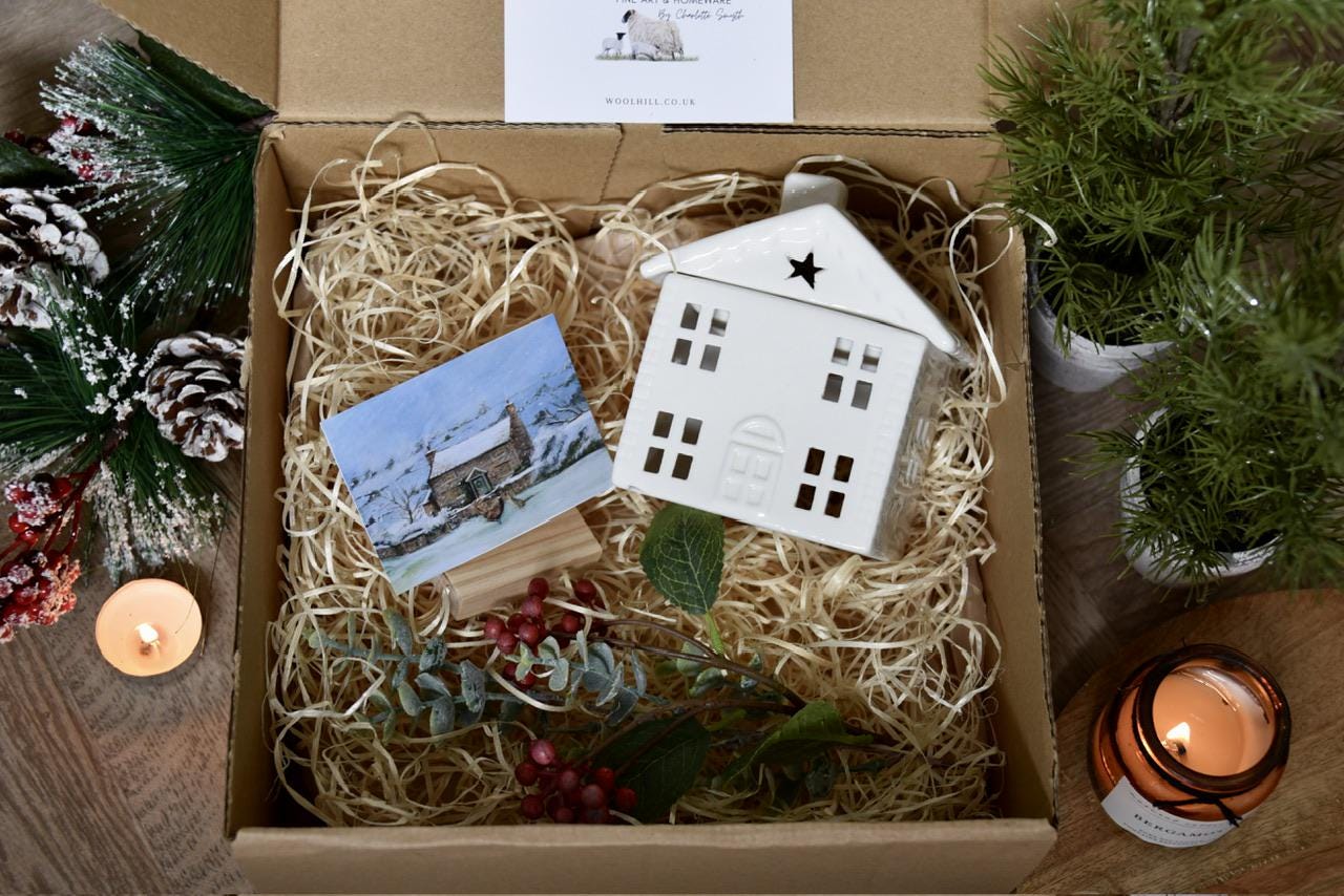 Decorative ceramic house and  cosy cottage print in a gift box with Christmas decor on a wooden floor.