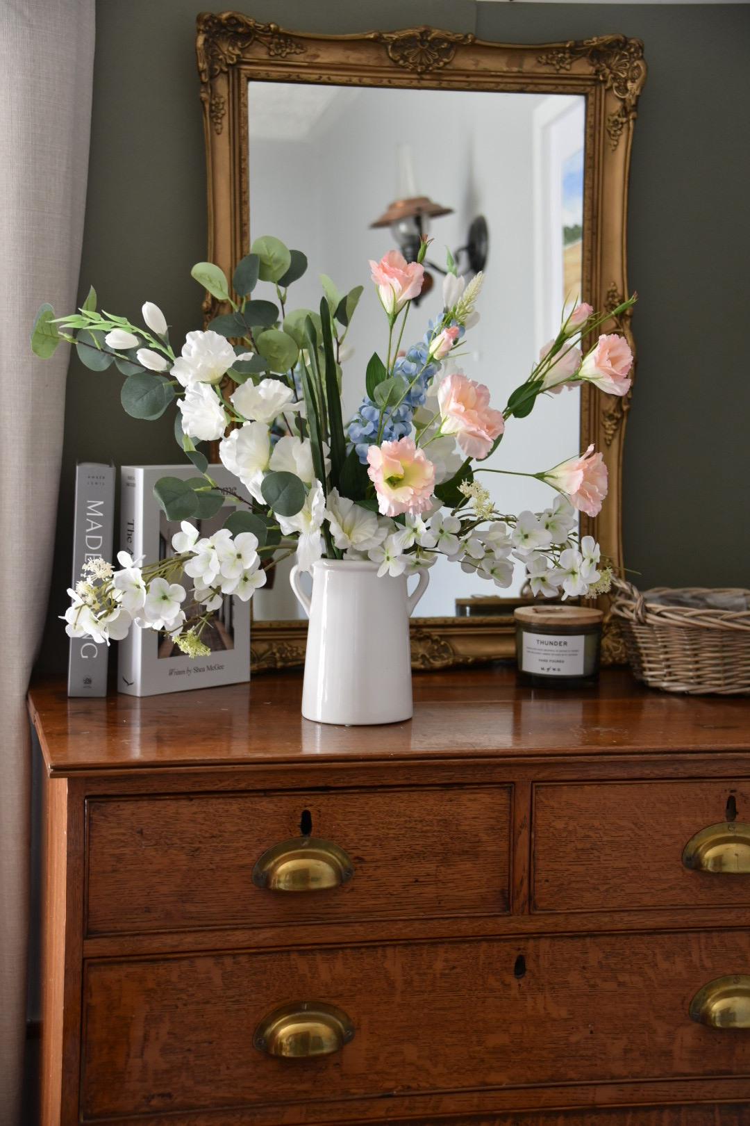 Wild flowers including gladiolus, wild white hydrangea, pink flowers, blue delphinium and green eucalytpus arranged in white vase on antique drawers